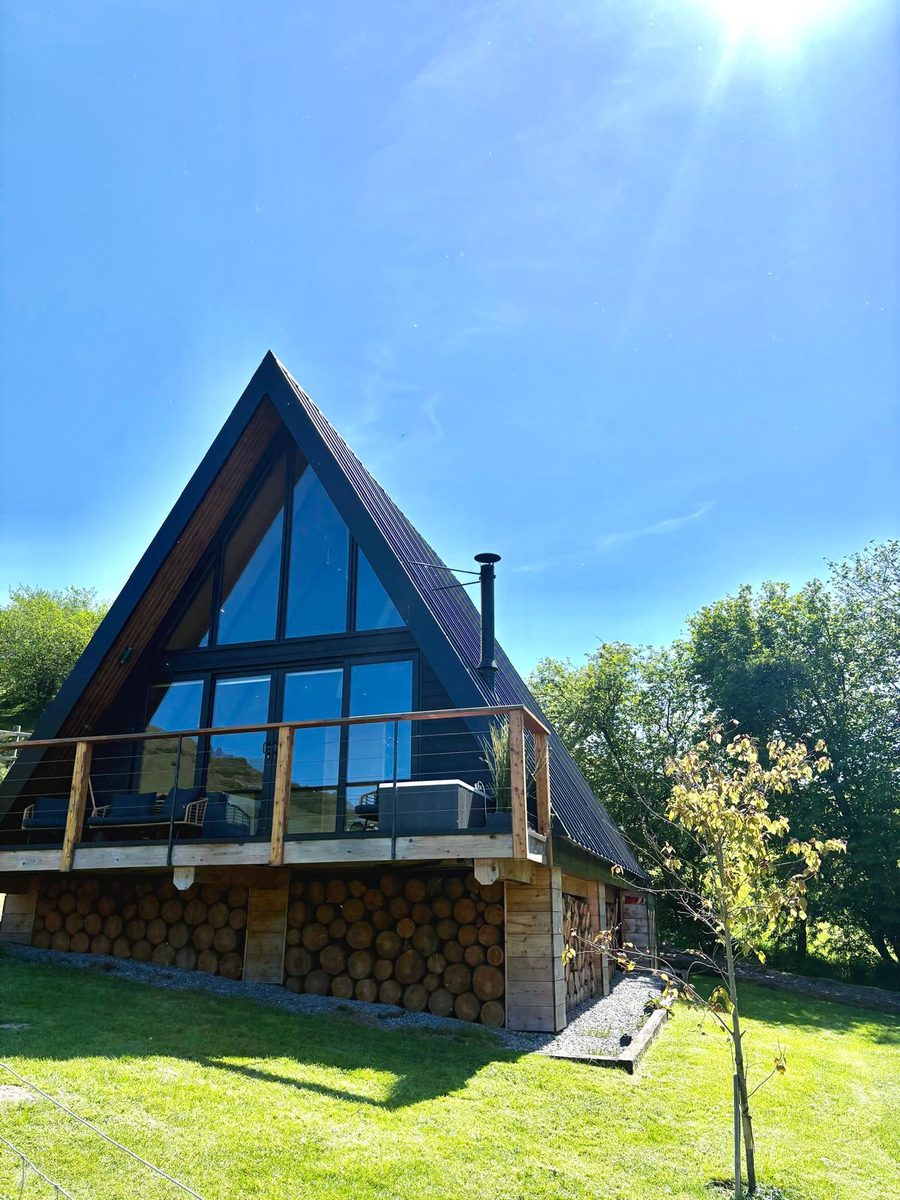 Triangular A-frame holiday lodge with floor-to-ceiling glazing under a clear blue sky