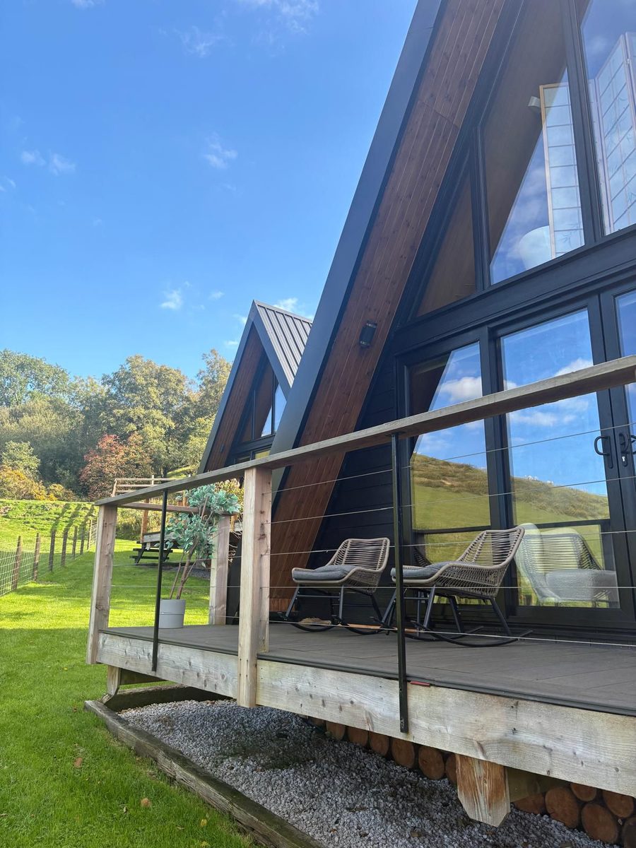 A-frame luxury holiday lodge with a glass frontage and decking, set in green countryside